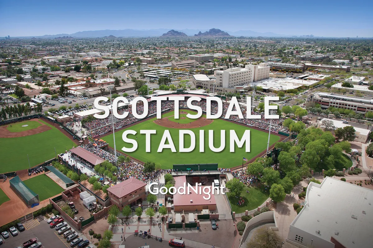 A lively scene of a baseball stadium set against scenic mountains, with a crowd of spectators enjoying the excitement of a live game. The stadium structure and vibrant atmosphere evoke the spirit of community sports events.