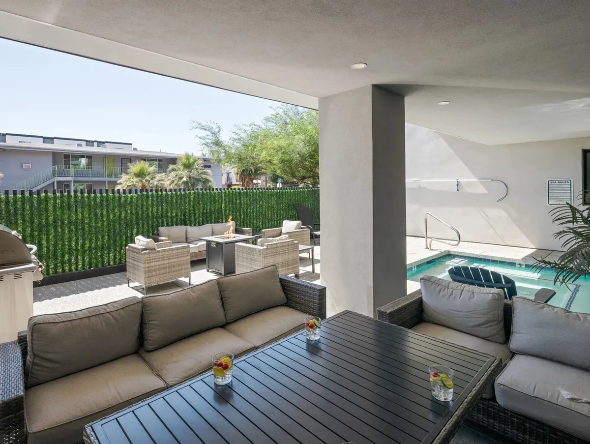 A stylish outdoor seating area adjacent to a sparkling swimming pool, surrounded by lush greenery and a dining table perfect for group gatherings. The scene is relaxed yet vibrant, inviting residents and guests to socialize, unwind, or enjoy a meal outdoors under the Arizona sky.