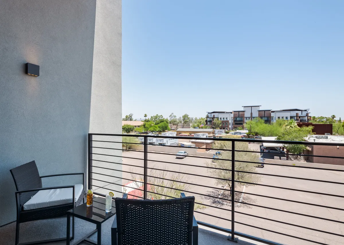 An exterior balcony with chairs, a small table, and a view of the surrounding area. The setting is perfect for morning coffee or evening drinks, blending the indoor living atmosphere with outdoor energy.